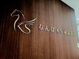 なんばKS泌尿器科・腎臓内科の院内ロゴサイン｜木目壁面に設置した真鍮切り文字サイン施工事例
